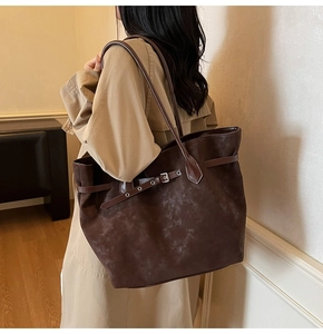 Detail view of large dark brown suede tote bag with adjustable buckle strap on model