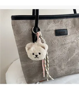 Close-up of gray tote bag with embossed cartoon animal patterns and plush bear keychain