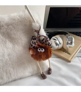 Détail d'un pendentif en peluche marron avec nœud léopard sur un sac à bandoulière blanc