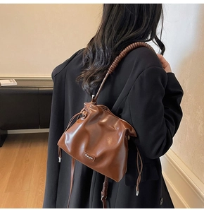 Detail view of brown leather bucket bag with pleated drawstring and textured spiral strap