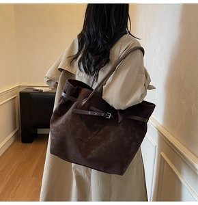Detail view of coffee brown suede tote bag with metal buckle strap on a shoulder