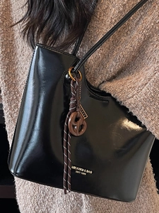 Minimalist black patent leather tote bag with elegant knot charm and gold logo lettering