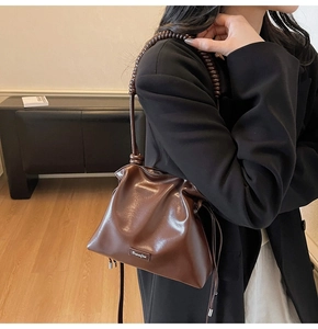Detail of vintage brown pleated bucket bag showing polished leather texture and spiral handle