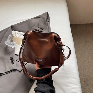 Close-up of brown bucket bag with thick knotted handle and metal logo detail