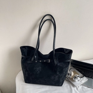 Detail of black matte leather tote bag featuring decorative strap and metal buckle
