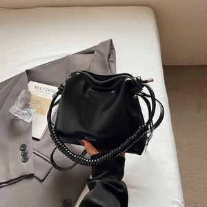 Detail of black drawstring bucket bag with spiral handle and adjustable strap on white bedding