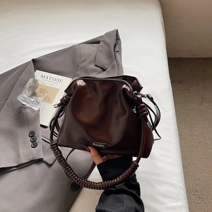 Detailed view of deep brown pleated bucket bag with spiral handle on aesthetic background