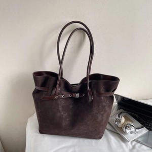 Detail of dark brown tote bag with matte texture and decorative belt in a lifestyle setting