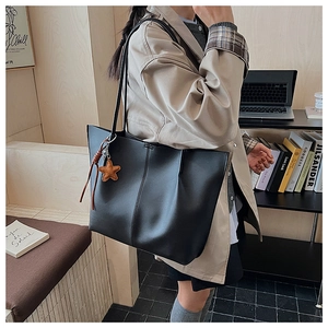 Detail shot of a large black leather tote bag with star charm worn in an office setting