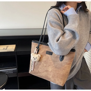 Detail showing brown tote bag with cartoon bear embossing and plush charm accessory