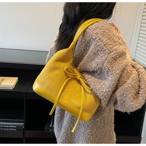 Détail du sac cabas en daim jaune avec nœud en cuir porté à l'épaule