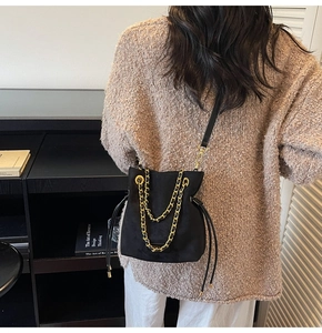 Détail d'un sac seau noir en daim avec chaînes dorées porté à l'épaule par un mannequin