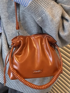 Brown leather drawstring bucket bag with spiral handle and crossbody strap for women