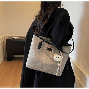 Close-up of gray embossed tote bag with cartoon patterns and white plush bear pendant