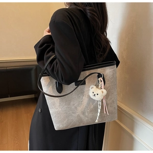 Detail of grey suede tote bag with cartoon bear embossing and white plush charm