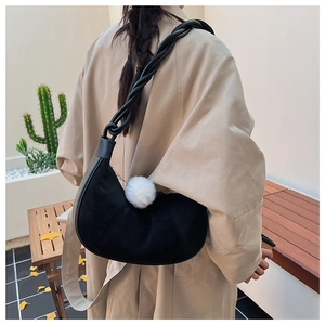 Detail of black crescent shoulder bag with woven strap and white pompom accessory