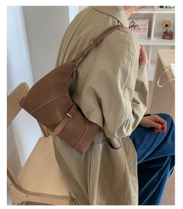 Detail of a brown crescent shoulder bag with white contrast stitching and metal buckle