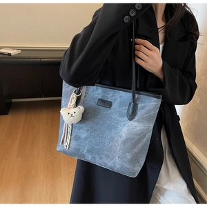 Detail of light blue denim tote bag with embossed bear pattern and plush bear charm