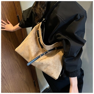 Detail of a large khaki suede tote bag with black straps worn by a model in a black jacket