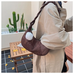 Detail of mocha brown suede crescent bag with twisted rope strap and white pompom charm
