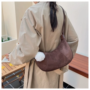 Detailed close-up of brown suede crescent shoulder bag with white plush ball charm