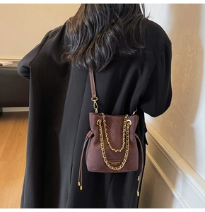 Détail du sac seau en daim marron rouge avec chaîne dorée et cordon de serrage