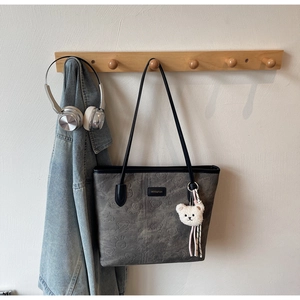 Detail of dark grey tote bag featuring bear and rabbit embossing with a plush charm