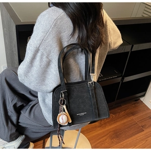 Close-up of black glossy handbag with shoulder strap and unique baseball pendant detail