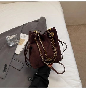 Détail du sac seau en daim marron foncé avec grosse chaîne dorée et cordon de serrage