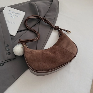 Detail of dark brown crescent bag with suede patchwork and woven strap with white pompom