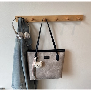 Detail of grey tote bag with embossed bear patterns and plush bear keychain on a hook