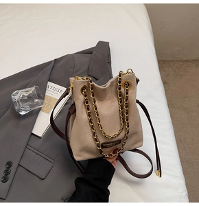 Détail du sac seau en daim beige avec chaîne dorée sur un blazer gris pour le quotidien