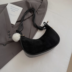 Detail of black suede crescent bag with white pompom on a stylish gray blazer