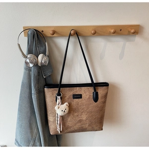 Detailed view of brown tote bag with bear embossing and plush charm hanging on a wall