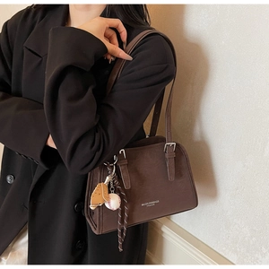 Close-up of brown suede shoulder bag featuring a stylish baseball charm and logo