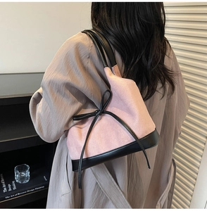 Détail d'un cabas en daim rose avec bordure en cuir noir et nœud papillon sur un modèle