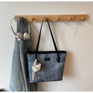 Detail of grey tote bag with bear pattern hanging with denim jacket and headphones