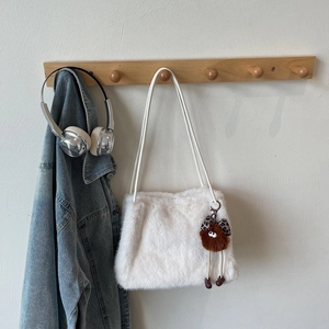 Détail d'un sac à bandoulière en peluche blanche avec un charm monstre sur cintre