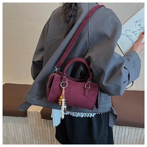 Detail showing burgundy suede crossbody bag with ethnic wood bead tassel on dark coat