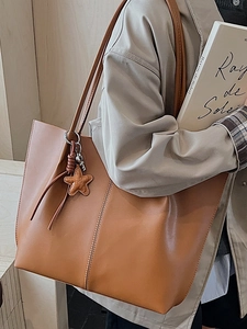 Minimalist large brown leather tote bag for women with star charm accessory on a model