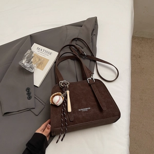 Detail of dark brown leather shoulder bag with baseball pendant and adjustable strap