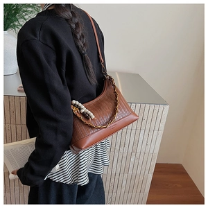 Detail der braunen geflochtenen Tasche mit Metallkette und Kunstharzperlen am Modell