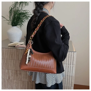 Detail der gewebten braunen Hobo-Tasche mit goldener Kette und buntem Perlen-Quasten