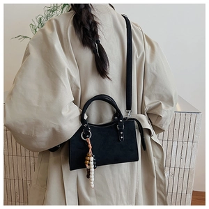 Detail of black crossbody bag with wooden bead charm and silver hardware on a beige coat