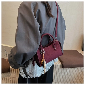 Detail of burgundy suede crossbody bag with wooden bead tassel shown on a model