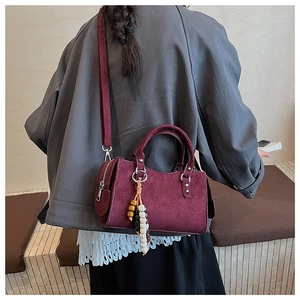 Detail view of burgundy suede handbag with elegant beaded charm and shoulder strap