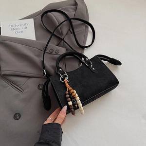 Close-up of black matte square handbag with wood bead charm and zipper detail