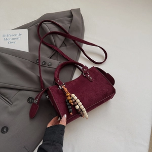 Detail of burgundy suede mini square bag with wooden bead charm on a grey suit jacket