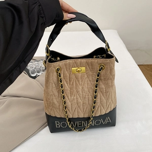 Detail of quilted brown and black leather bucket bag with gold chain and metal logo