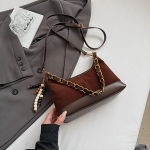 Detail der braunen Wildledertasche mit goldener Kette und Holzperlen-Quasten auf einem Blazer